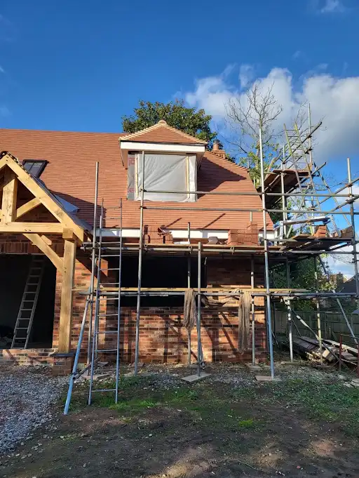 Brick house under construction with scaffolding and a window covered by a tarp on the roof.