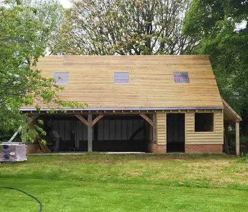 Wooden house under construction with a large front open area and three small windows on the roof.