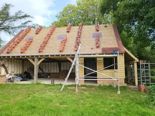 Partially constructed wooden roof with rows of tiles and scaffolding in front of a building under renovation.
