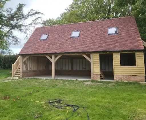 Wooden garage or barn with three skylights on the roof and open bays on grass lawn.