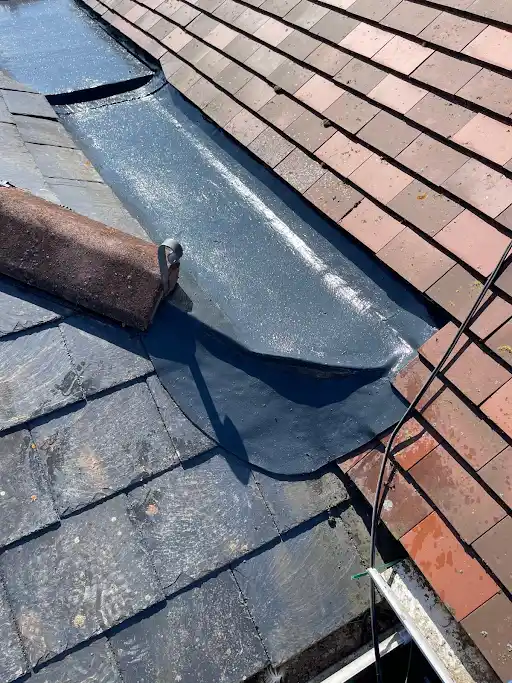 Roof valley with red tiles on one side and dark slate tiles on the other, showing waterproof flashing.