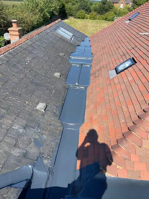Conjoined rooftops with black slate and red tiles separated by metal flashing, shadow of person visible.