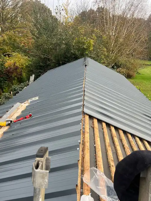 Partially installed gray metal roof panels on wooden battens with trees and grass in background.