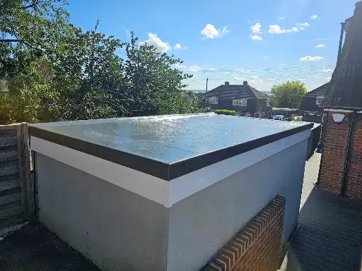 Flat concrete garage roof with black trim beside a brick house under a blue sky with clouds.
