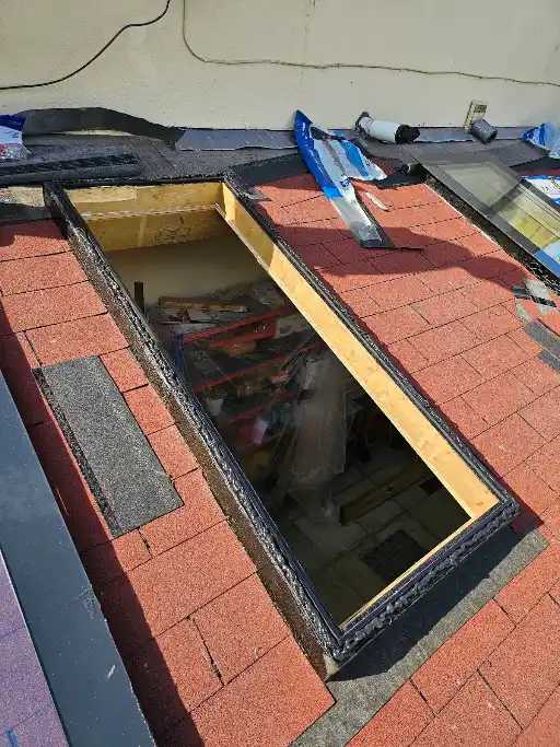 A roof window frame being installed in a red shingle roof under daylight.