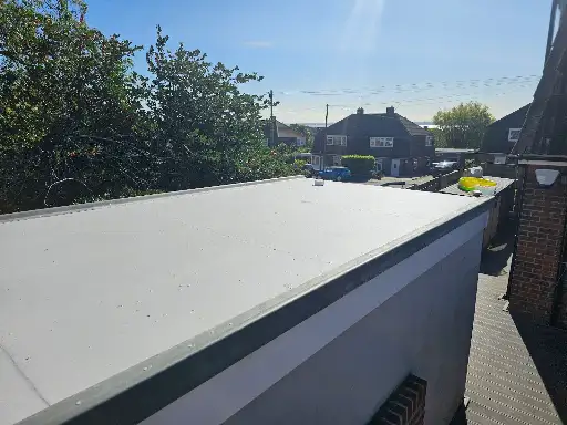 Flat white rooftop under clear blue sky with trees and houses in the background.