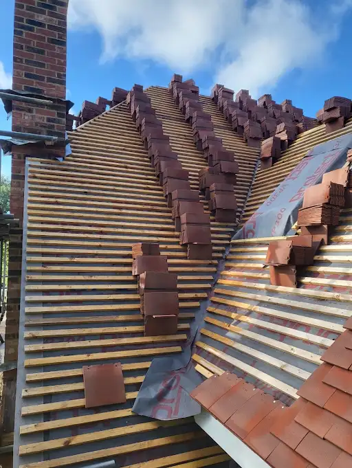 Partially tiled sloped roof under construction with rows of wooden battens and stacked clay tiles.