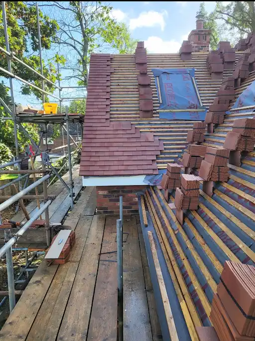 Partially tiled roof under construction with stacks of bricks and scaffolding on the side.