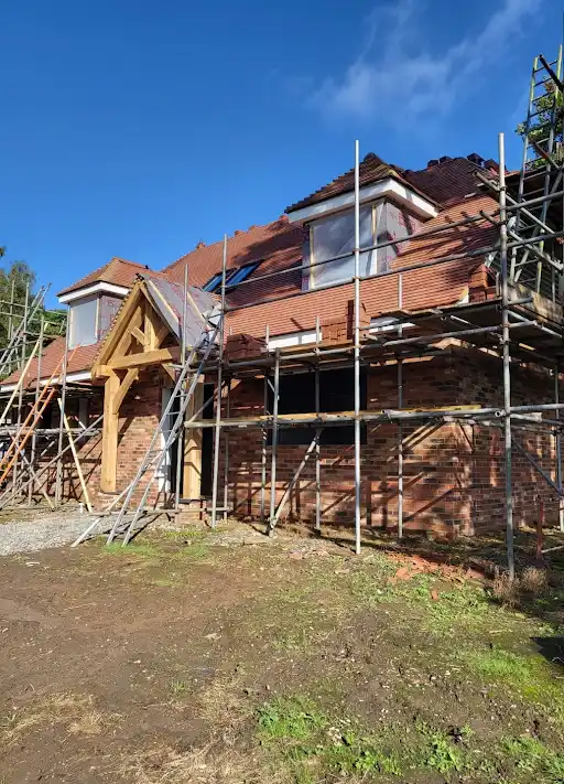 Two-story brick house under construction with scaffolding on front and roof on a clear day.