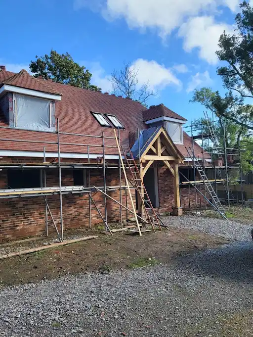 Brick house under roof construction with scaffolding and ladders against a blue sky with clouds.
