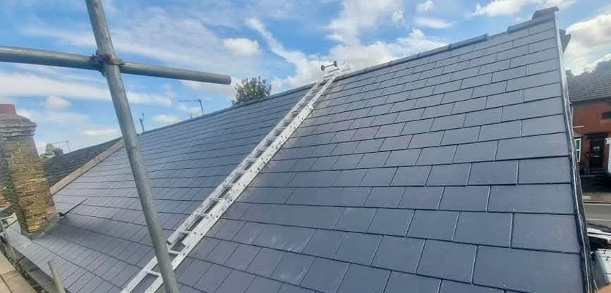 Newly installed dark slate roof on a house with a ladder leaning against it under blue sky.
